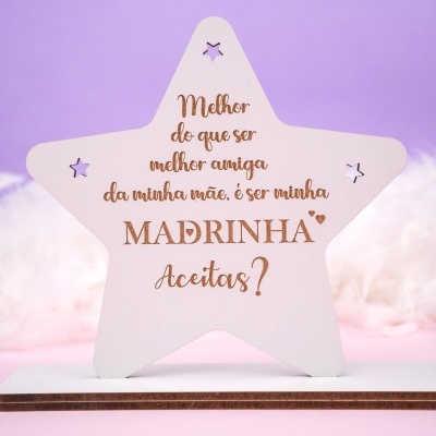 Estrela decorativa clara com texto gravado a laser contra fundo lilás.