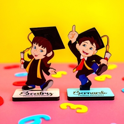 Figuras caricaturais de formandos com diplomas e bonés sobre base com nomes e fundo colorido