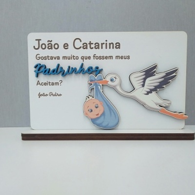 Placa branca com texto e ilustração de cegonha a transportar bebé envolto em pano azul