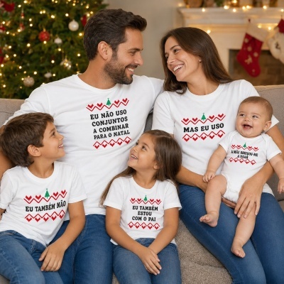 Família com camisolas e babygrow brancas com mensagens de Natal em português, sentada em sofá com árvore de Natal ao fundo.