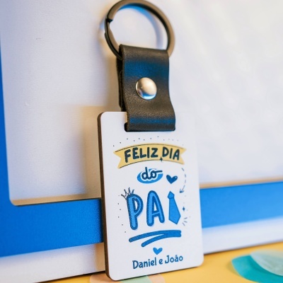 Porta-chaves com cinta preta em pele e placa branca com texto e ilustrações