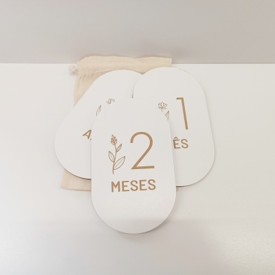 Cartões brancos com números dourados e ilustrações de folhas sobre fundo branco e bolsa de pano bege.