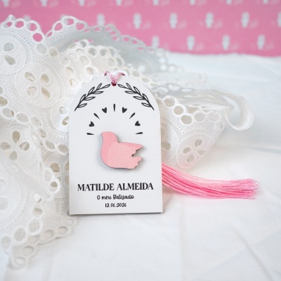 Etiqueta branca com passarinho rosa sobre renda branca e pano rosa ao fundo