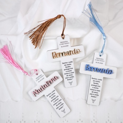 Cruzes decorativas em cartão branco com nomes dourado, azul e rosa e tassels coloridos.