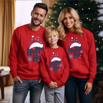 Três pessoas com camisolas vermelhas natalícias com texto Ho Ho Ho e gorro de Pai Natal, em ambiente com árvore de Natal