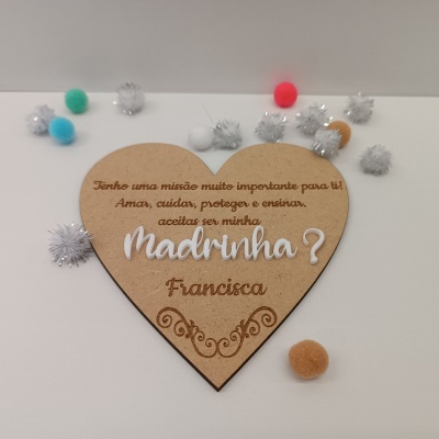 Placa de madeira em forma de coração com texto gravado e pompons coloridos em fundo branco