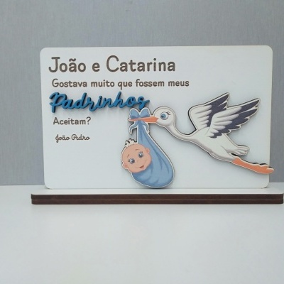 Quadro branco com tecido azul, cegonha e texto sobre pedido de padrinhos