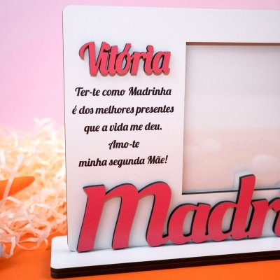 Moldura branca com nome em relevo vermelho e texto em preto numa decoração com fundo rosa.