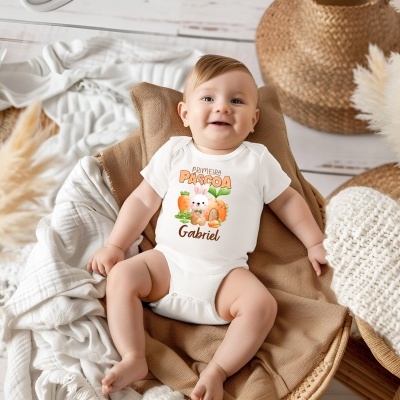 Bebé sorridente com bodysuit branco decorado com coelho e texto sobre fundo de almofada castanha e mantas brancas.