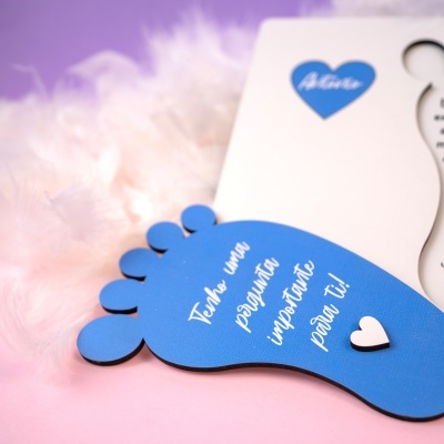 Placa decorativa azul em forma de pé com texto em branco e corações sobre fundo rosa e penas brancas