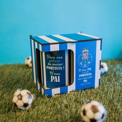 Caixa azul e branca de FC Porto com texto em português e bolas de futebol em miniatura num fundo de relva.