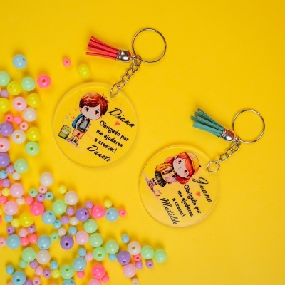 Dois porta-chaves redondos de acrílico com ilustrações de crianças e mensagens de agradecimento em português, com franjas coloridas, sobre fundo amarelo com pérolas.