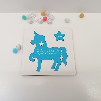 Convite de papel branco com silhueta azul de unicórnio e texto em português com pompons coloridos ao redor.