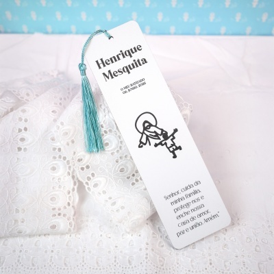 Marcador de livro branco com franja azul pendurado em tecido branco bordado