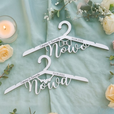 Cabides brancos personalizados para noivo e noiva sobre tecido verde claro com flores e vela
