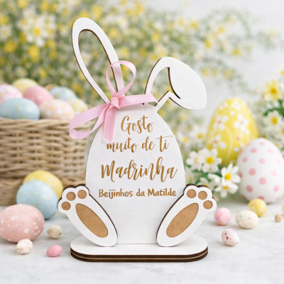 Decoração de coelho em madeira branca com texto e laço cor-de-rosa junto de ovos de páscoa coloridos