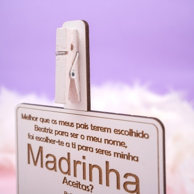 Pregador de roupa branco segurando cartão de madeira com texto em fundo lilás.
