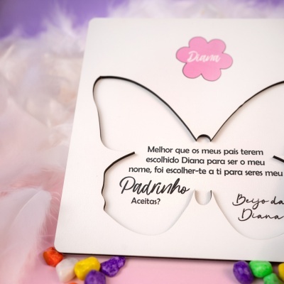Convite em papel branco com recorte em forma de borboleta e texto em português, com uma etiqueta rosa em forma de flor com o nome Diana