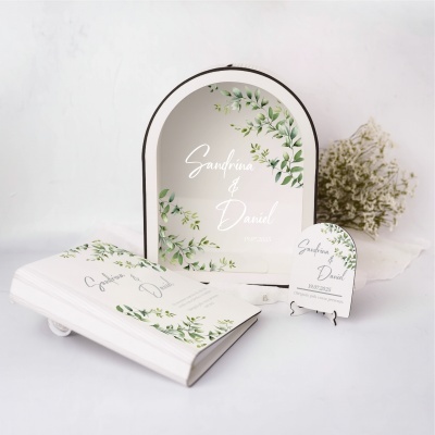 Convite e cartão com design de folhas verdes e texto Sandrina & Daniel 19.07.2025 ao lado de espelho com moldura branca e decoração semelhante.