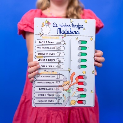 Quadro de tarefas infantil com texto e ilustrações coloridas segurado por uma criança
