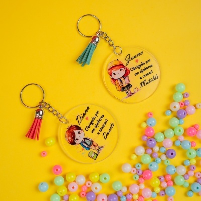 Porta-chaves redondos personalizados com desenho de criança e texto em português sobre fundo amarelo com bolas coloridas.