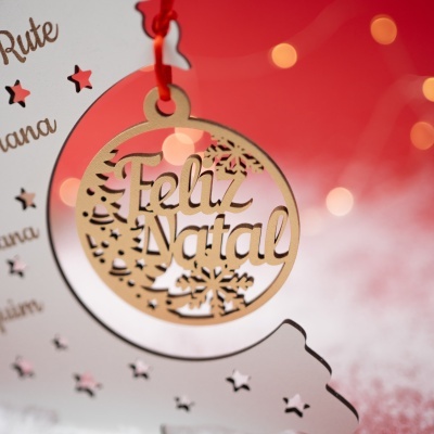 Ornamento de Natal em madeira clara com inscrição Feliz Natal pendurado por fita vermelha
