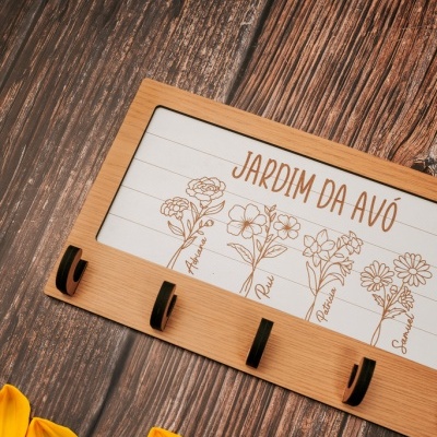 Base de madeira com ganchos e quadro branco decorado com nomes e flores, sobre superfície de madeira escura e pétalas amarelas ao lado.