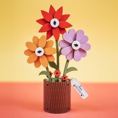 Vaso decorativo com flores coloridas em madeira e etiqueta em fundo amarelo e coral