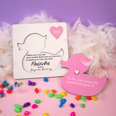 Cartão de convite em forma de pato com recorte e texto em português e outro pato rosa com texto, decorados com penas brancas e pedras coloridas em fundo lilás e rosa.