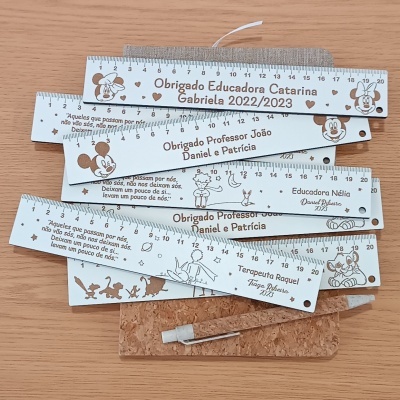 Réguas brancas personalizadas com desenhos e textos em castanho, sobre mesa de madeira, com estojo de cortiça e lápis.