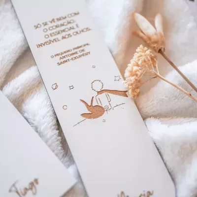 Marcador de livros branco com texto e ilustração do Pequeno Príncipe sobre tecido branco felpudo e flores secas