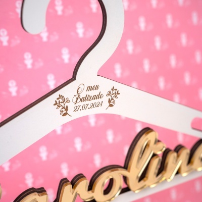 Cabide branco com texto gravado e fundo rosa com padrão branco.