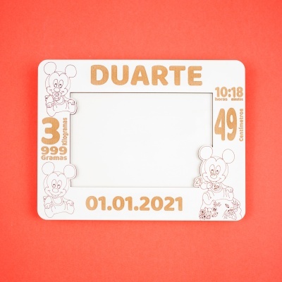 Moldura branca de madeira com desenhos Mickey e texto gravado, sobre fundo laranja.