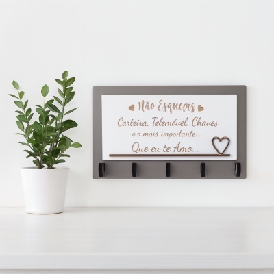 Suporte de parede com ganchos e placa decorativa ao lado de planta em vaso.