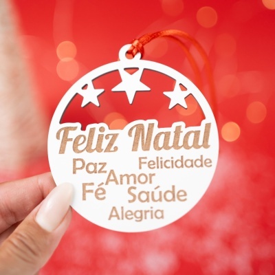 Enfeite de Natal redondo em madeira clara com palavras em relevo e estrelas recortadas, suspenso por fio vermelho