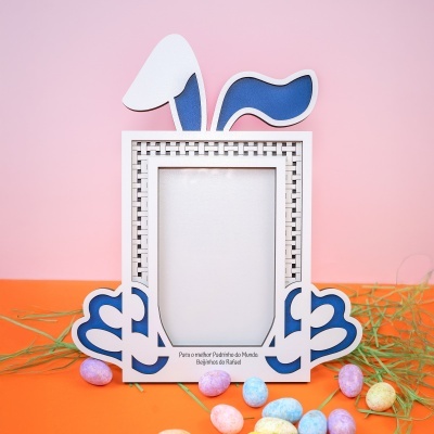 Moldura de madeira decorativa com orelhas e patas de coelho azuis em fundo rosa e ovos coloridos