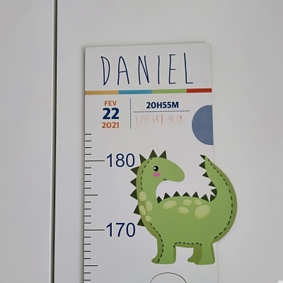 Régua de crescimento branca com dinossauro verde e dados de nascimento escritos.
