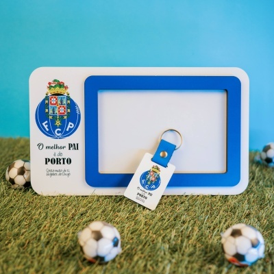 Moldura branca e azul com chaveiro e mini bolas de futebol sobre relva sintética.