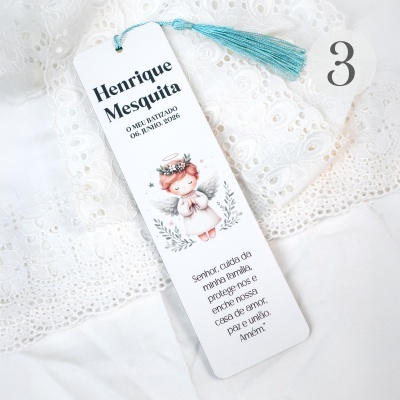 Marcador de livros branco com tassel azul e anjinho sobre tecido branco rendado.