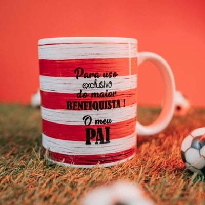Caneca com riscas vermelhas e brancas e texto para benfiquista, numa relva com bola de futebol