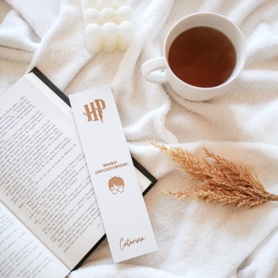 Marcador de livros branco HP com chá, vela branca e ramo seco sobre manta branca e livro aberto