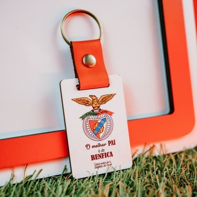 Chaveiro vermelho com placa branca e brasão, texto em português, sobre relva artificial