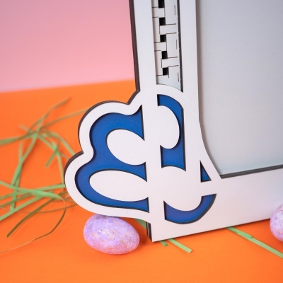 Objeto decorativo branco com recortes entalhados em azul azul, ovos roxos e fundo laranja e rosa