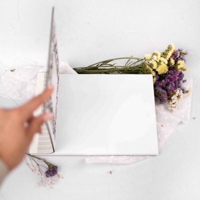 Livro aberto com capa branca junto a flores secas sobre tecido branco