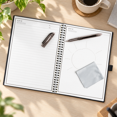 Caderno aberto, caneta, pano para limpeza, xícara de café e planta sobre mesa de madeira