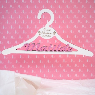 Cabide branco para batismo com nome Matilda em letras cor-de-rosa, fundo rosa com padrão branco religioso.