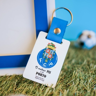 Porta-chaves em couro azul com etiqueta branca e selo colorido sobre relva artificial
