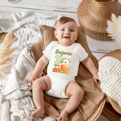 Bebé com body branco estampado Benjamin 3 meses sentado em almofada castanha