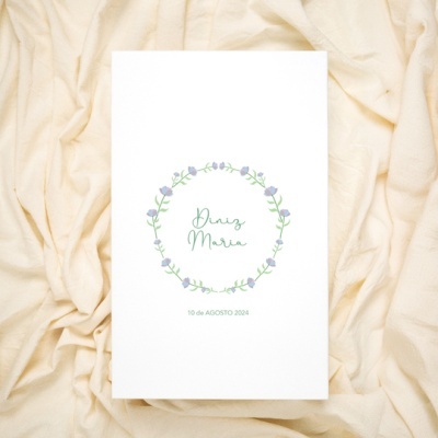 Convite branco com coroa de flores e texto verde sobre tecido bege claro