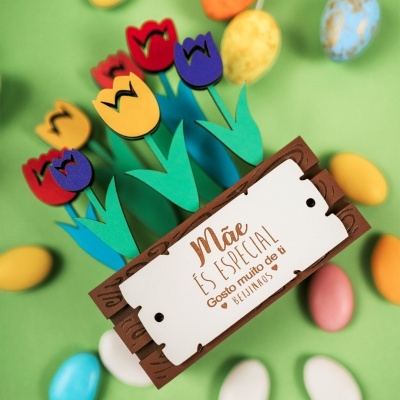 Cartão decorativo com flores de papel coloridas e mensagem em português sobre fundo verde com amêndoas coloridas